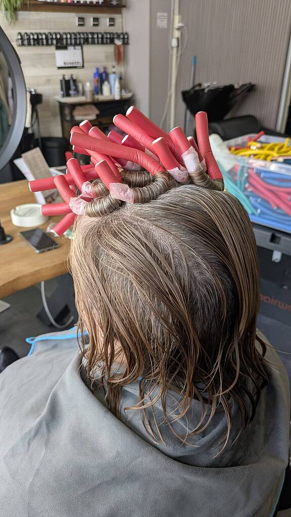 Vrouw krijgt haarstyling met rode haarrollers in een salonomgeving.