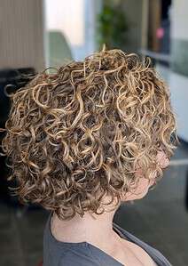 Krullend, gekruld haar met blonde highlights op een vrouw in een kapsalon.