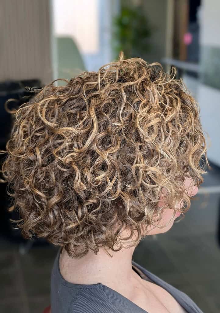 Krullend, gekruld haar met blonde highlights op een vrouw in een kapsalon.